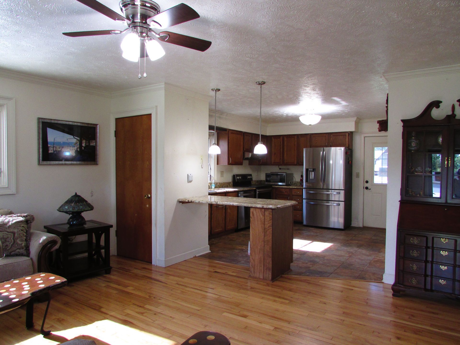 Open-plan living room and kitchen with hardwood floors, ceiling fans, and wood cabinets