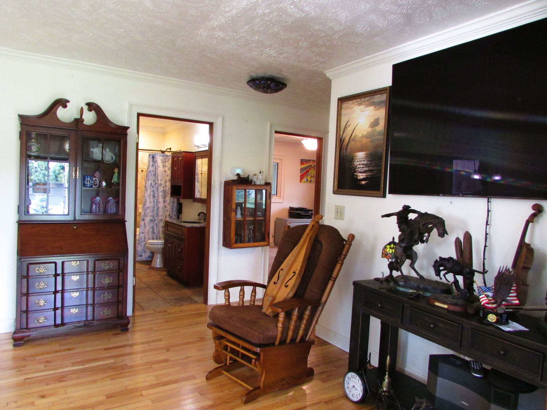 Living room with hardwood floor, wooden furniture, rocking chair, and a large TV mounted on the wall