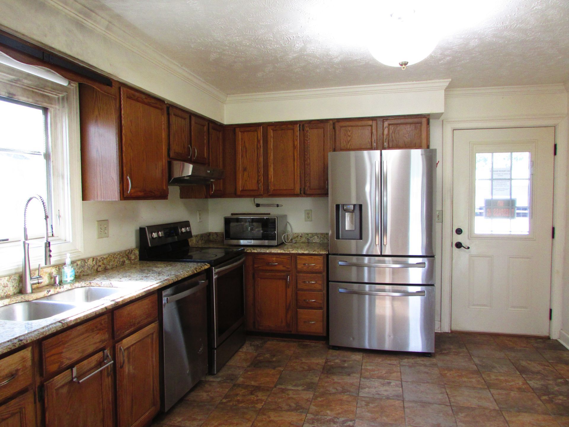 Kitchen with wood cabinets, stainless appliances, granite counters, and tile floor, lit by a ceiling light