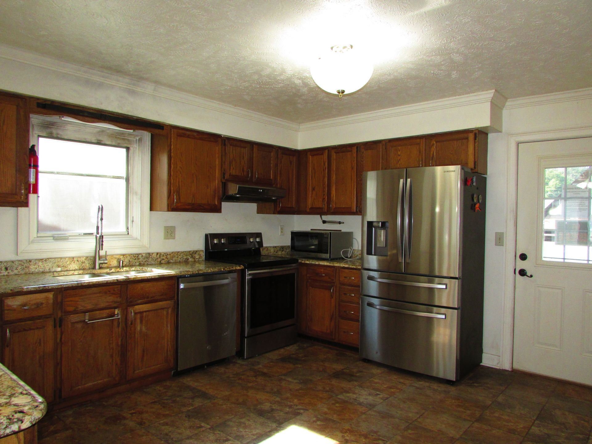 Kitchen with wooden cabinets, stainless steel refrigerator, black appliances, and a white door by the counter.