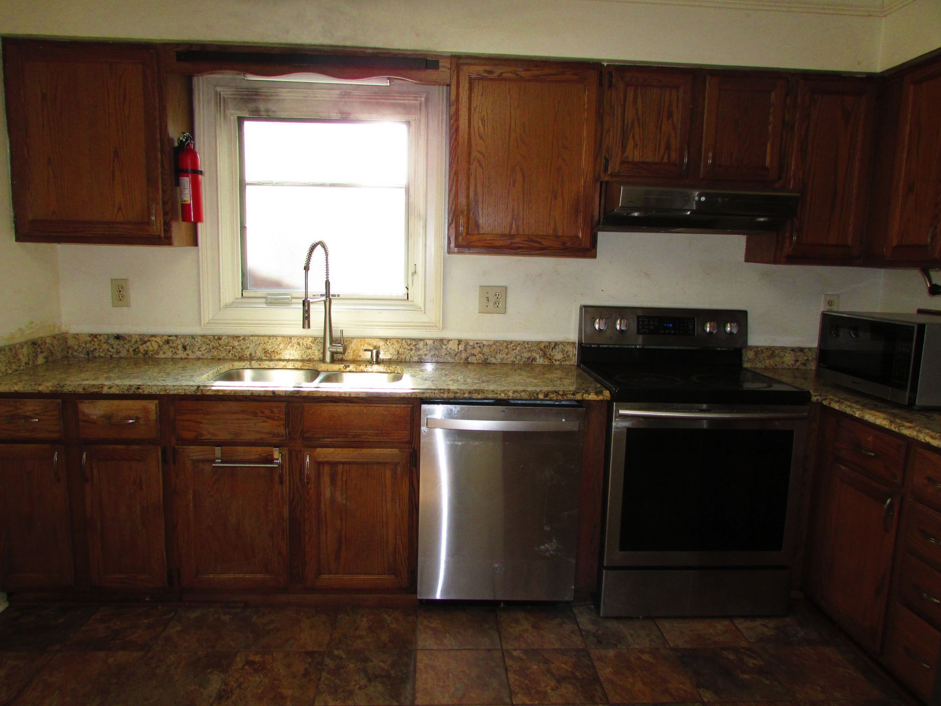 Kitchen with wooden cabinets, granite counters, window over sink, dishwasher, stove, and microwave