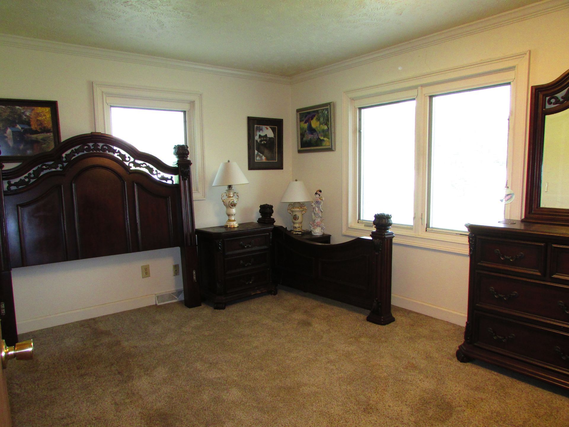 Spacious bedroom with dark wood furniture, beige carpet, and windows letting in daylight