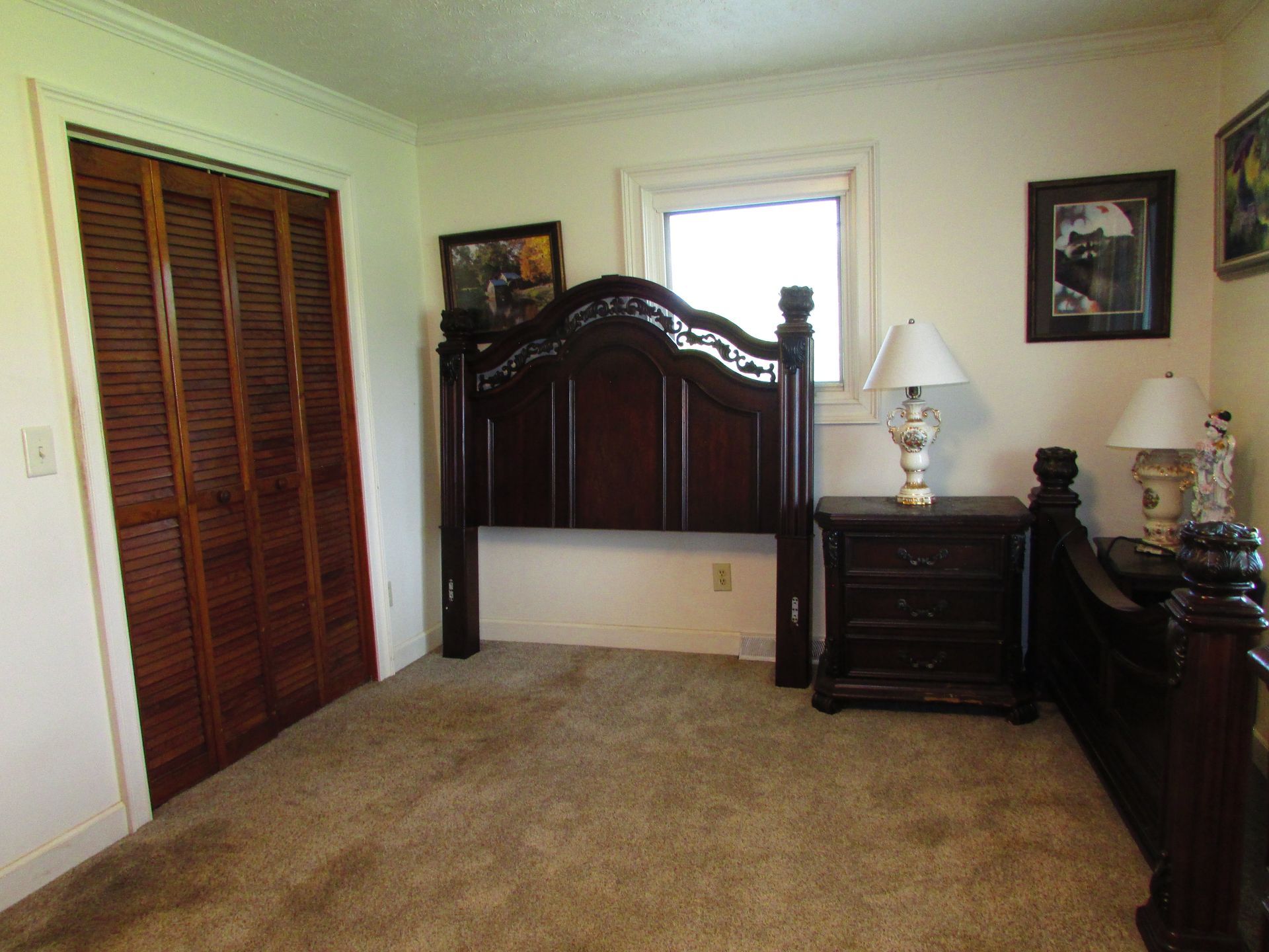 Bedroom with dark wood bed frame, nightstands, lamp, and closet doors on carpeted floor.