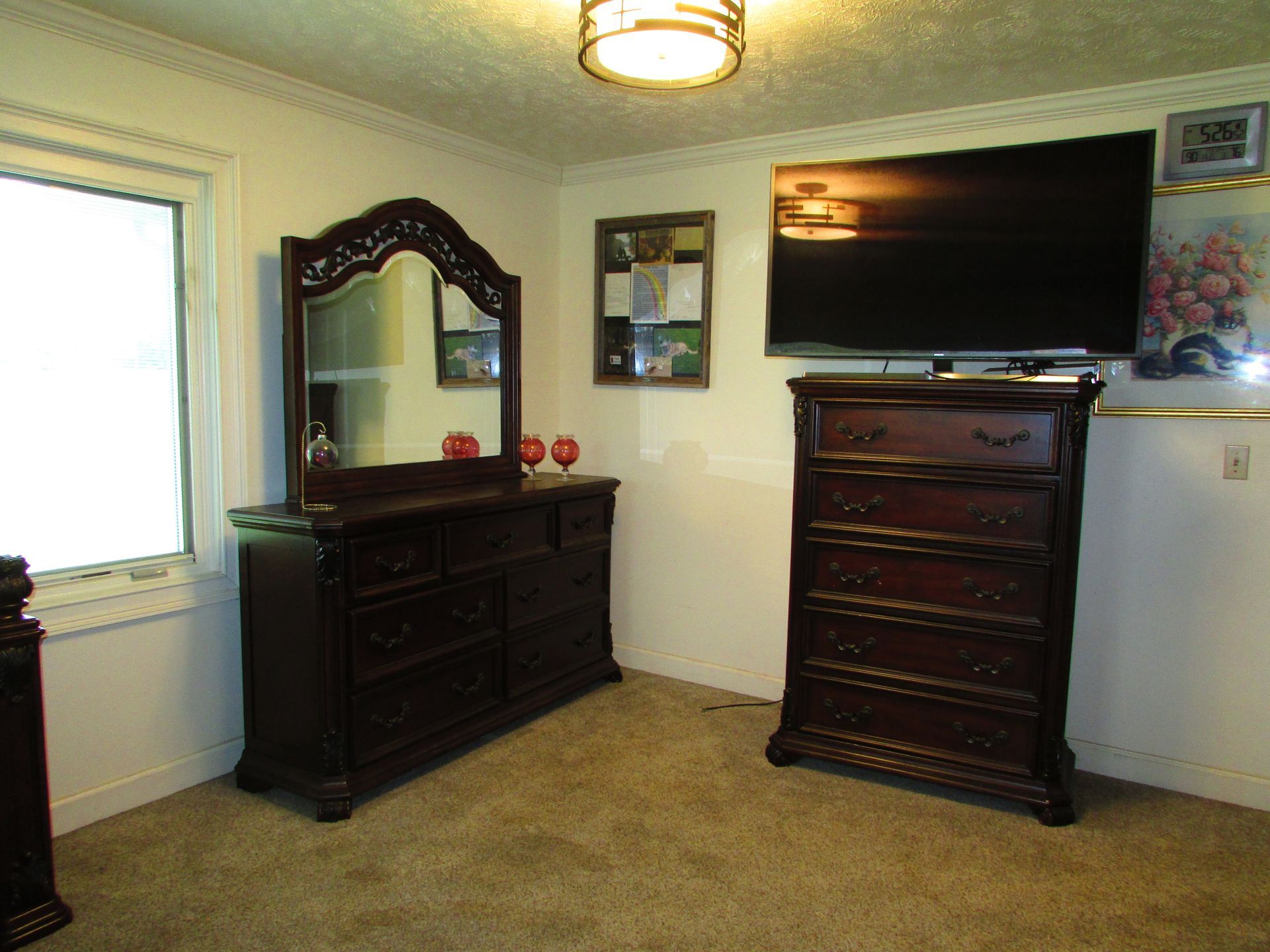 Bedroom with dark wood dresser and mirror, chest of drawers, wall-mounted TV, and beige carpet.