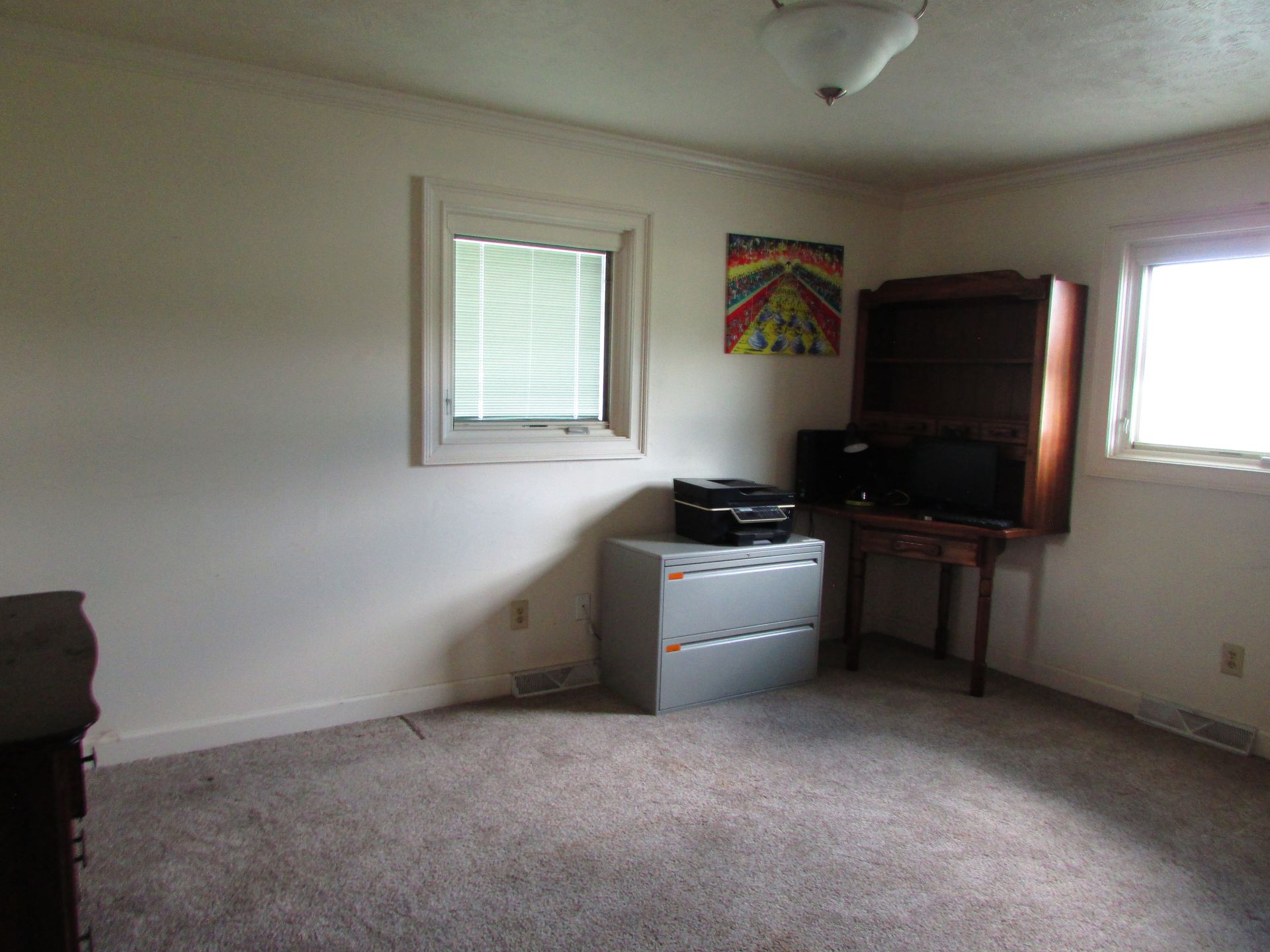 Empty beige living room with carpet, small windows, and a TV stand in the corner