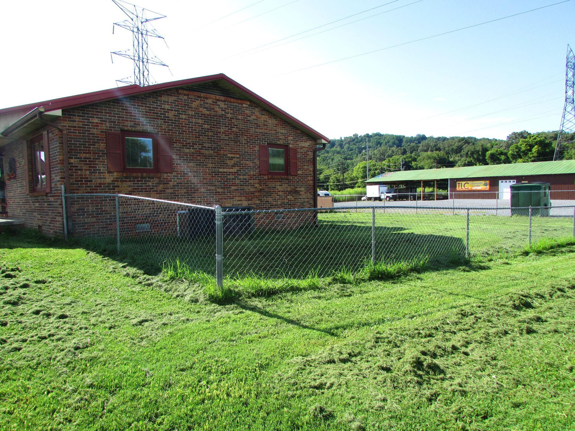 Brick building with fenced grassy yard under a clear sky, near power lines and a road