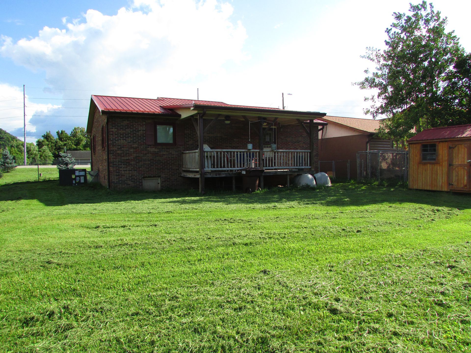 Rural brick house with red roof and porch, sitting beside a wide green lawn under a bright sky