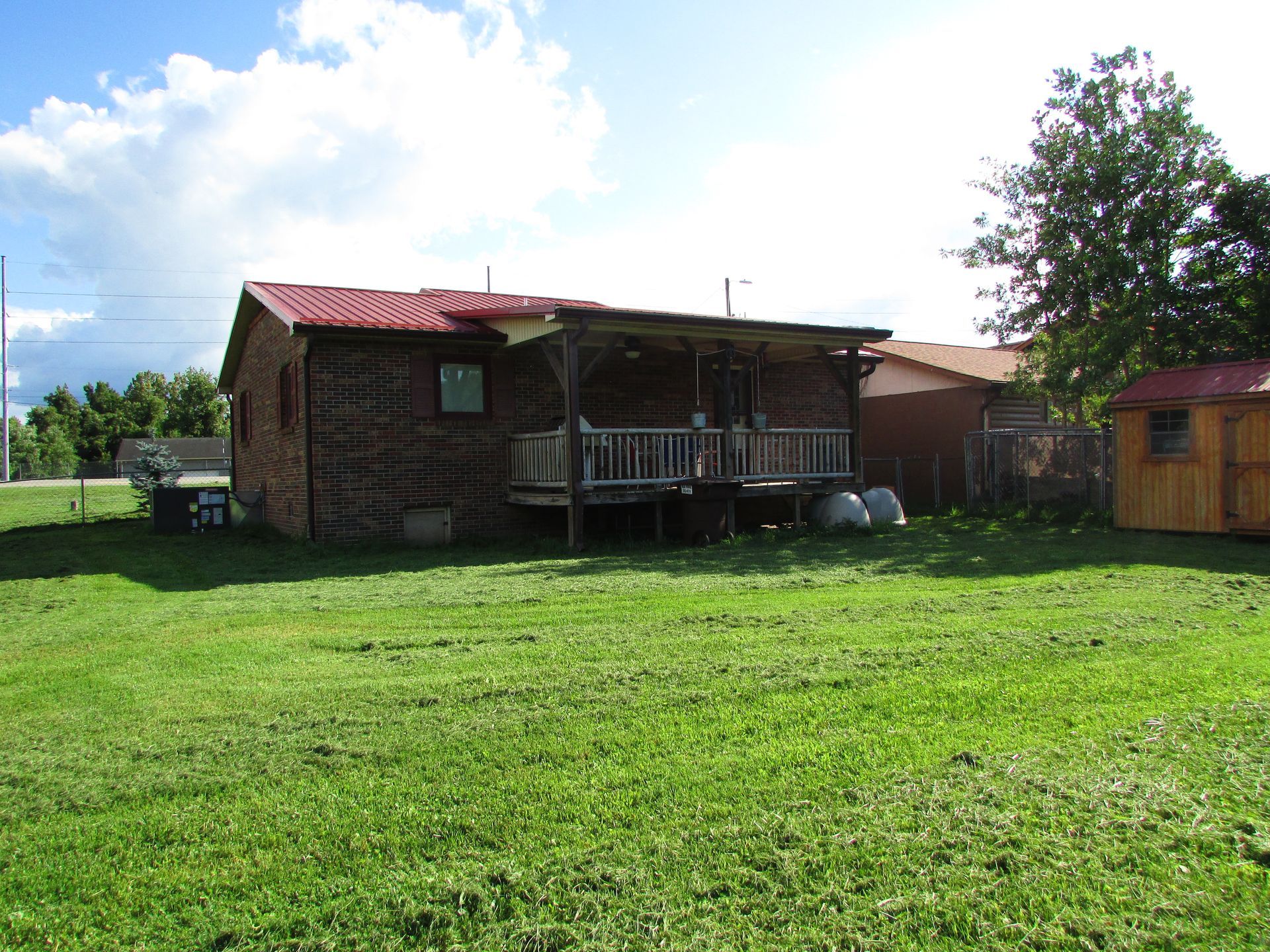 Small brick cabin with a red roof in a grassy field under a bright sky