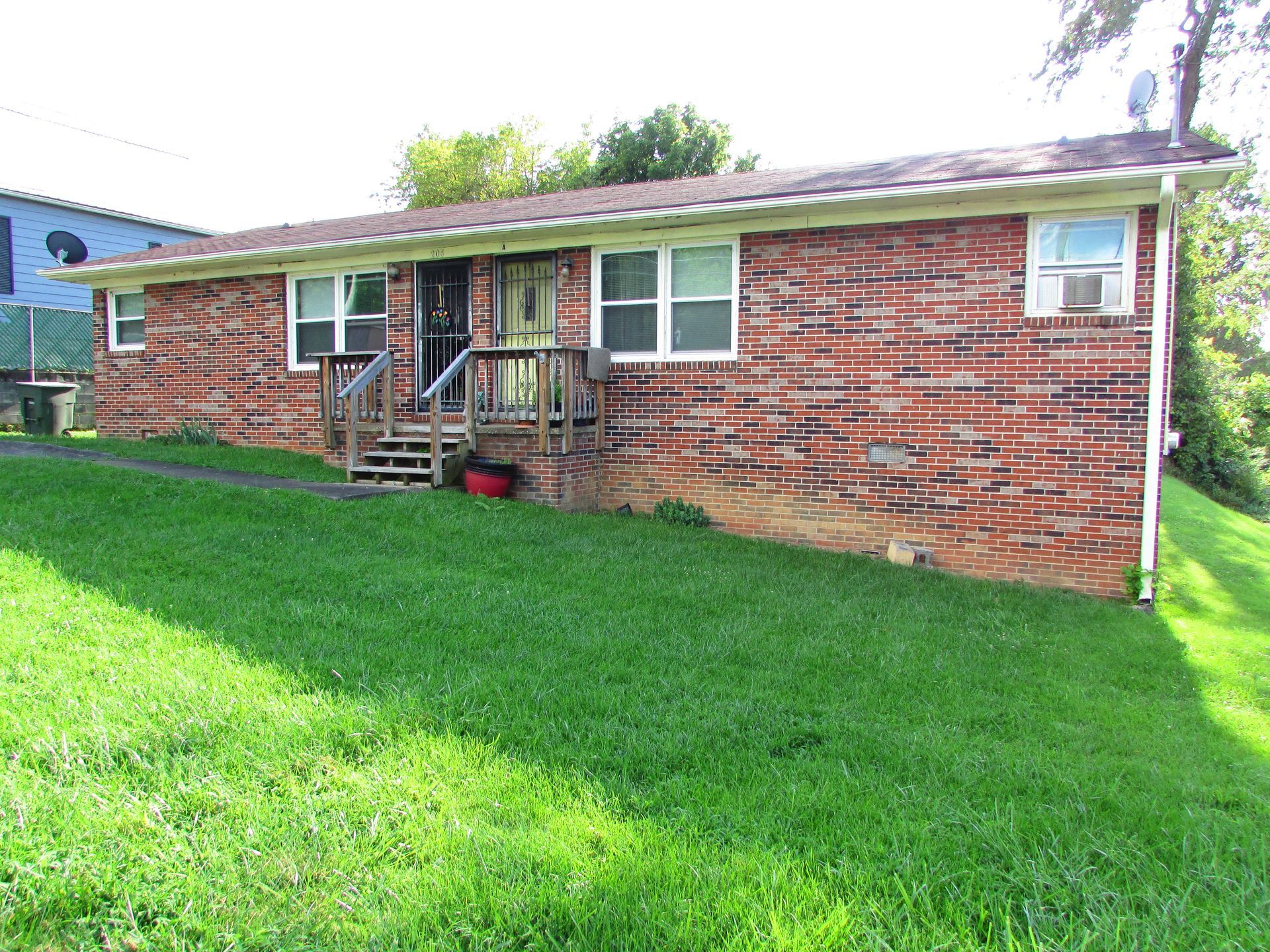 Brick house with a small front porch and steps, set behind a bright green lawn.