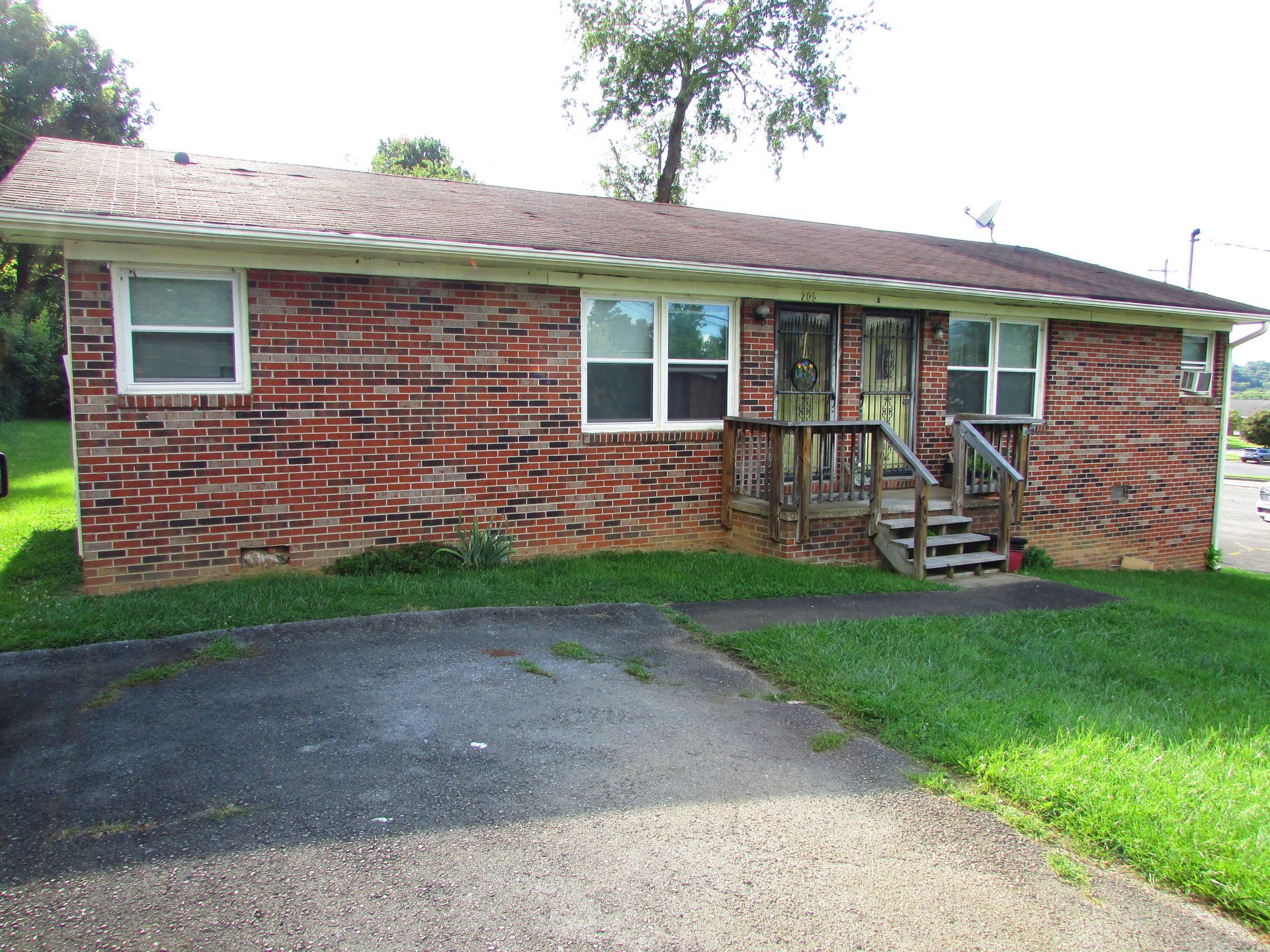 Brick house with small front porch, windows, and a paved driveway beside a green lawn