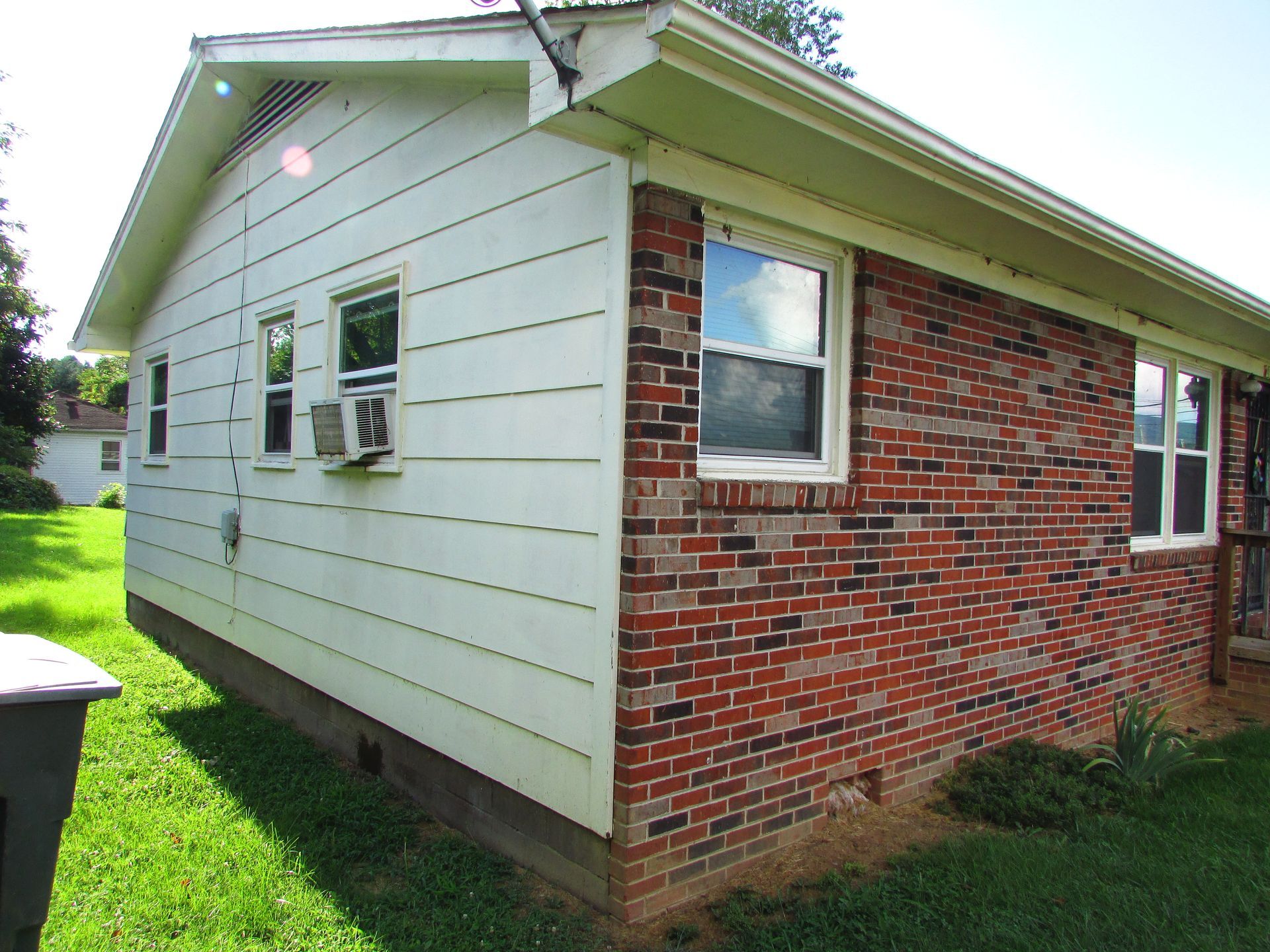 Side view of a small white-and-red brick house with a grassy yard and windows.
