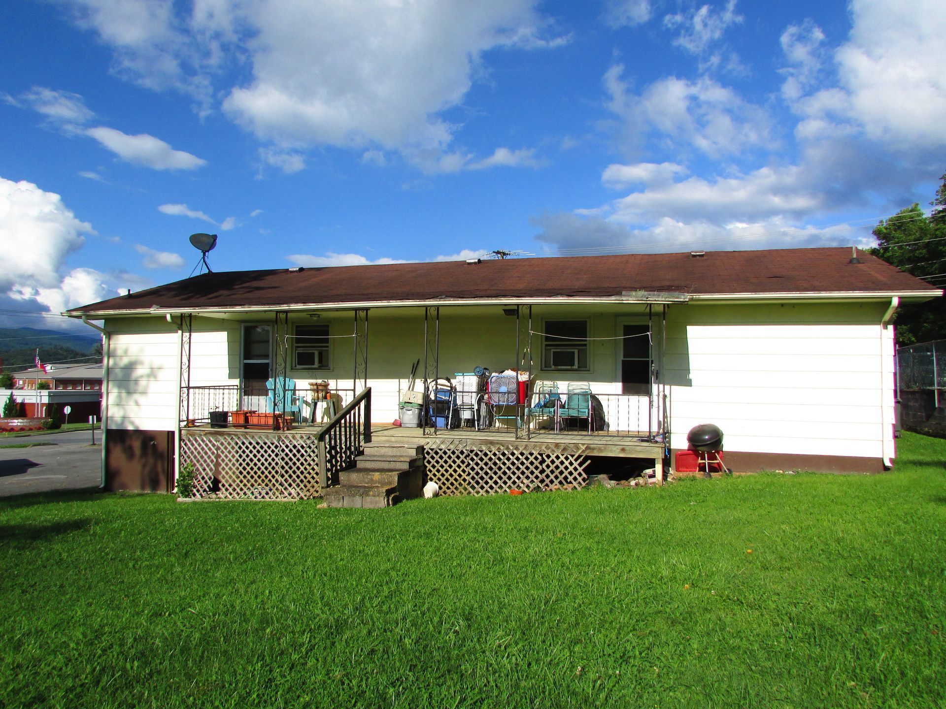 Single-story white house with a red roof and porch, set behind a bright green lawn under a blue sky.