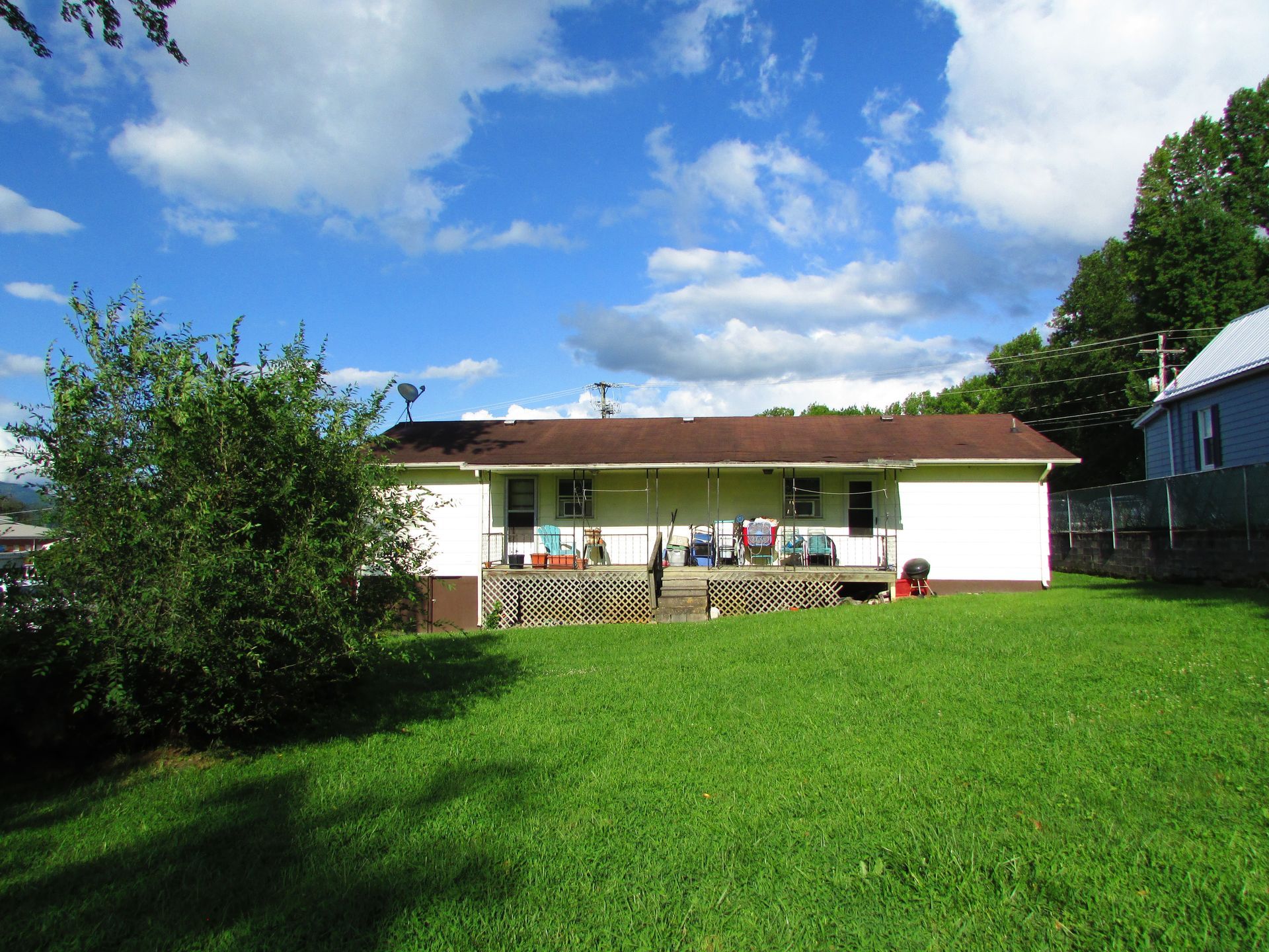 White house with red roof and small porch behind a large green yard under a blue sky
