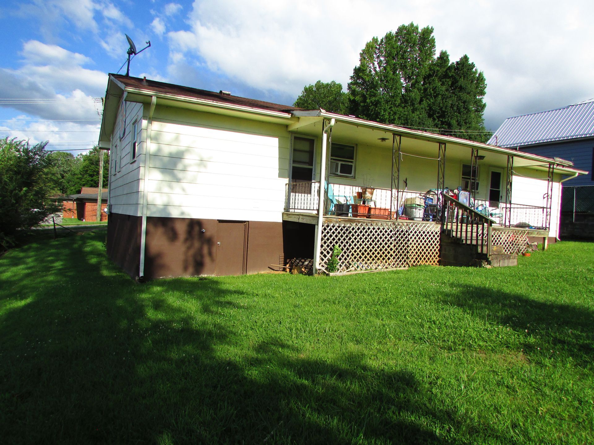 Single-story white house with brown trim, front porch, and green lawn under a partly cloudy sky