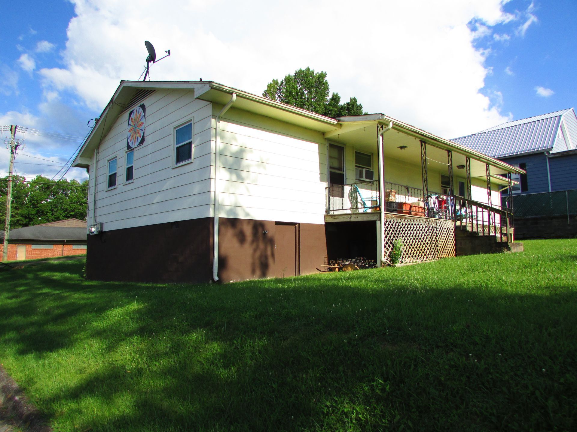 White house with brown foundation and covered porch on a grassy hill under a blue sky