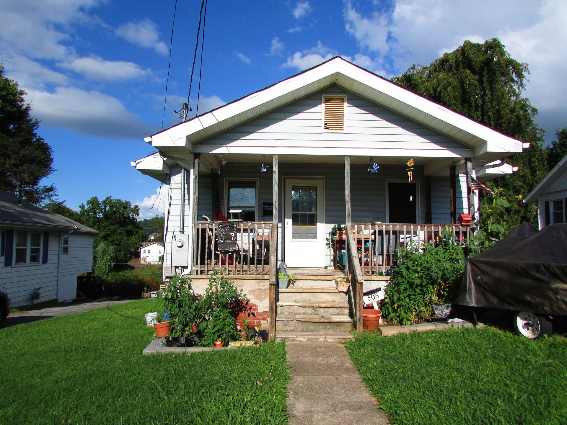 Small white bungalow with front porch, steps, and flower beds on a sunny day