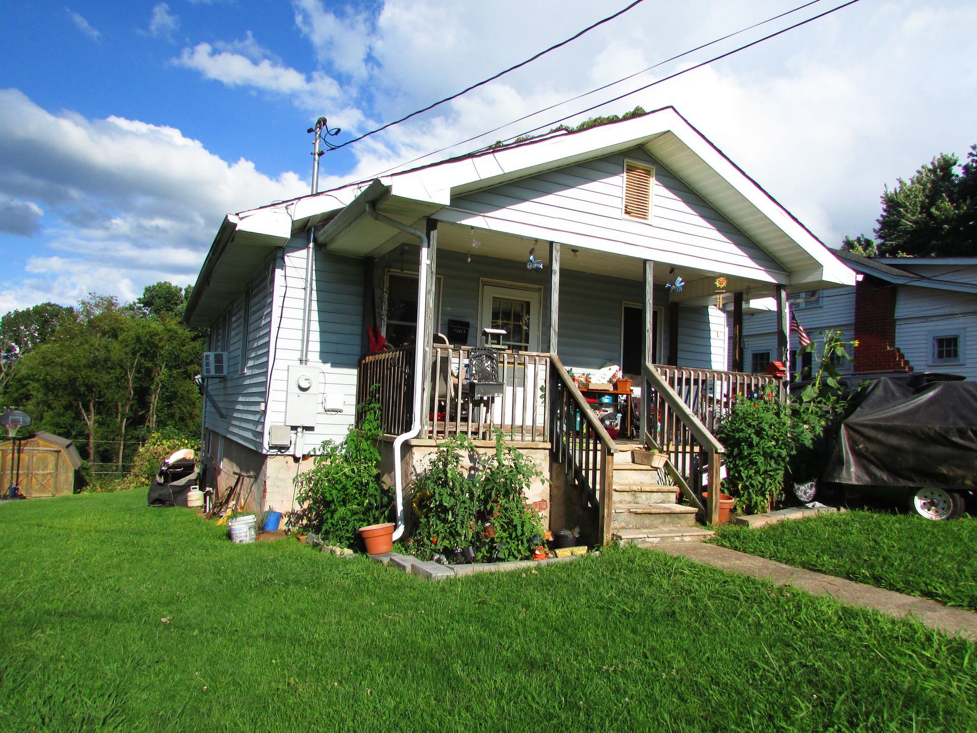 Small white house with a front porch, steps, and a green lawn under a partly cloudy sky