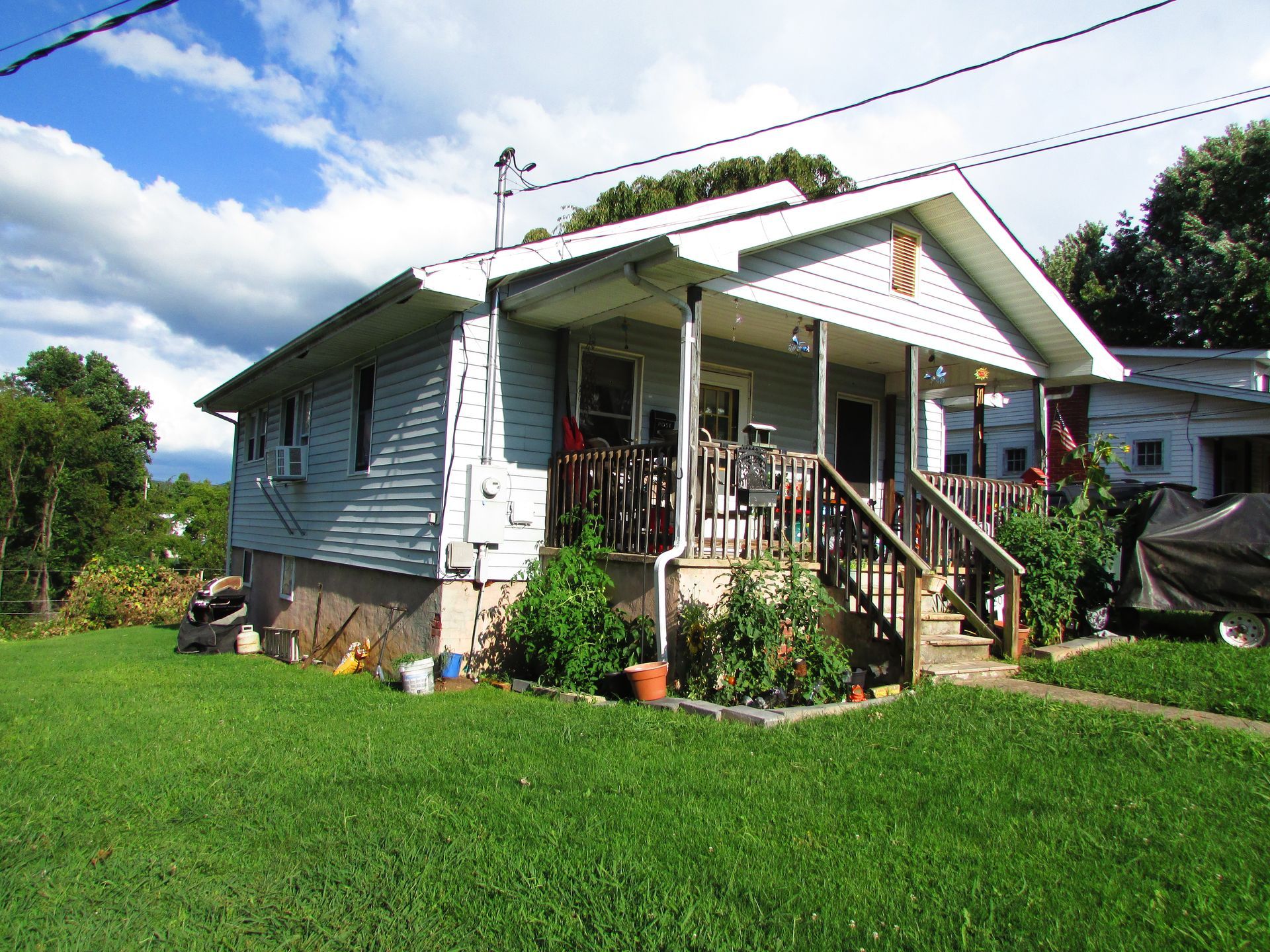 Small white house with a front porch and steps, set on a green lawn under a partly cloudy sky