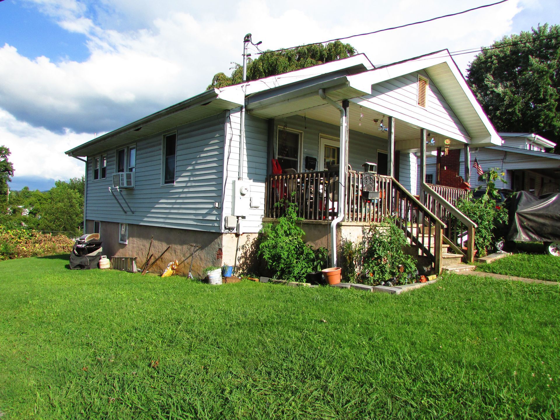 Small blue house with a front porch and steps, set in a green yard under a partly cloudy sky