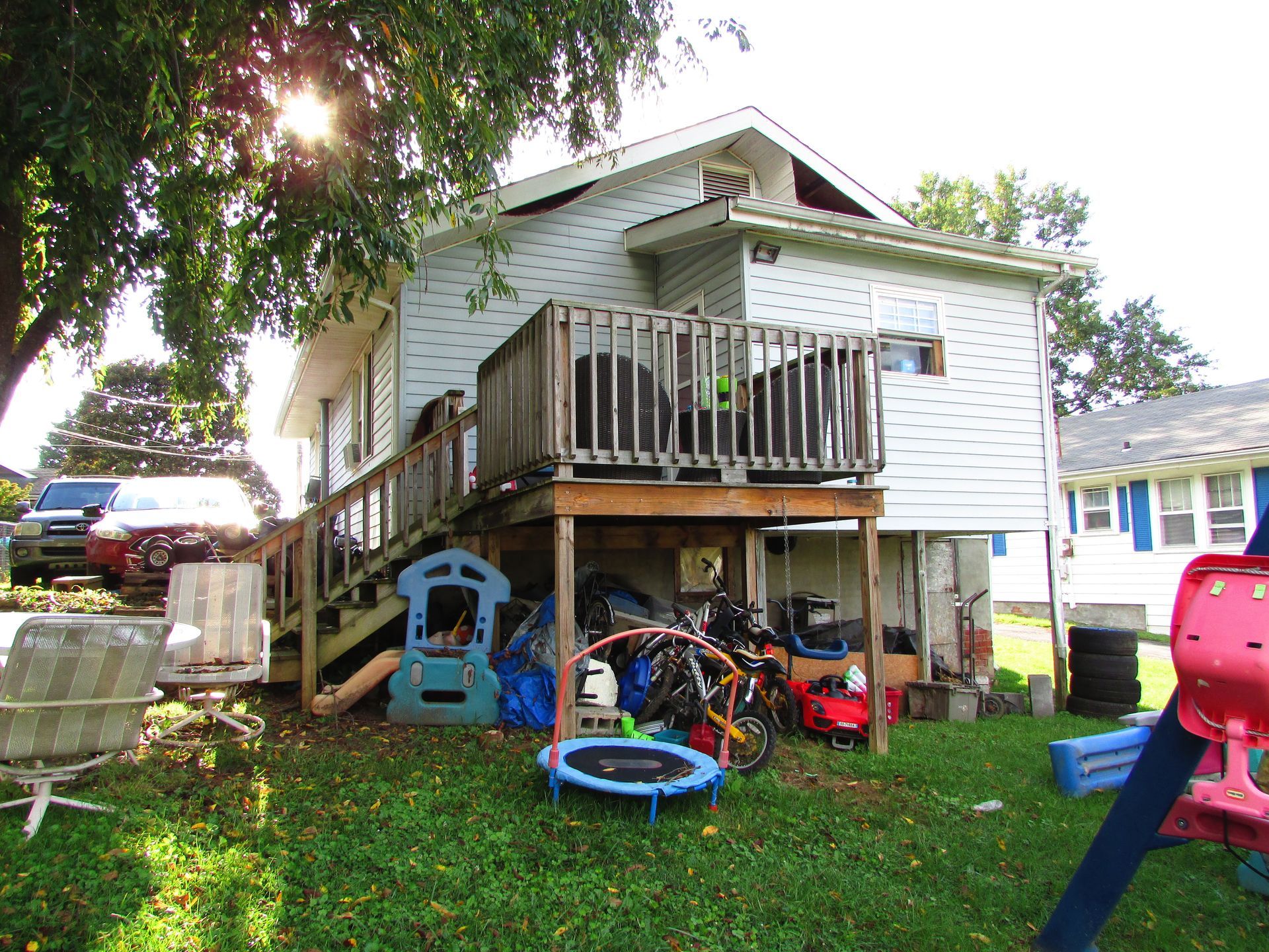 Backyard with a white house, wooden deck, stairs, and children’s toys on the grass.