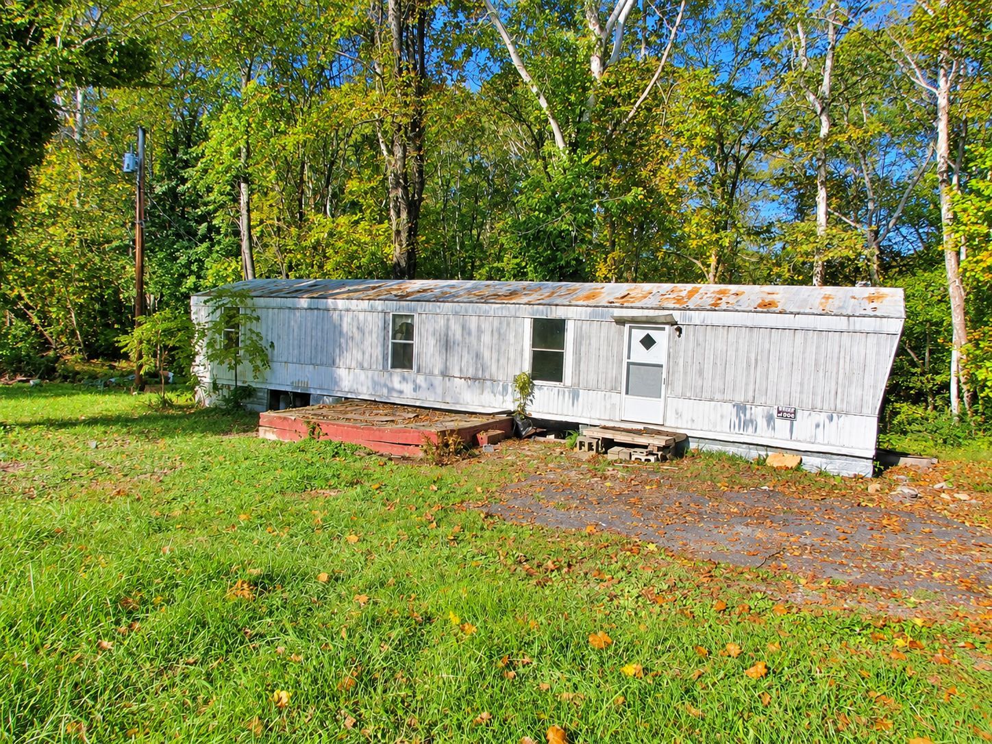 White mobile home on a grassy lot surrounded by trees under a bright blue sky