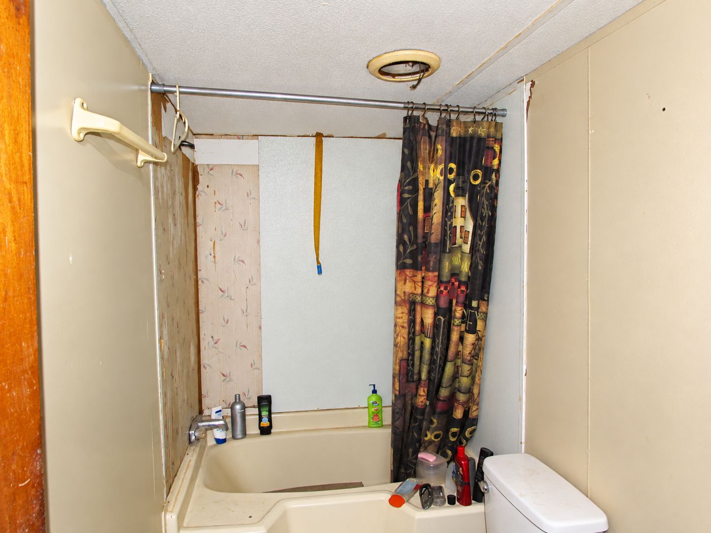 Small bathroom with a bathtub, shower curtain, beige walls, and toiletries on the tub edge.