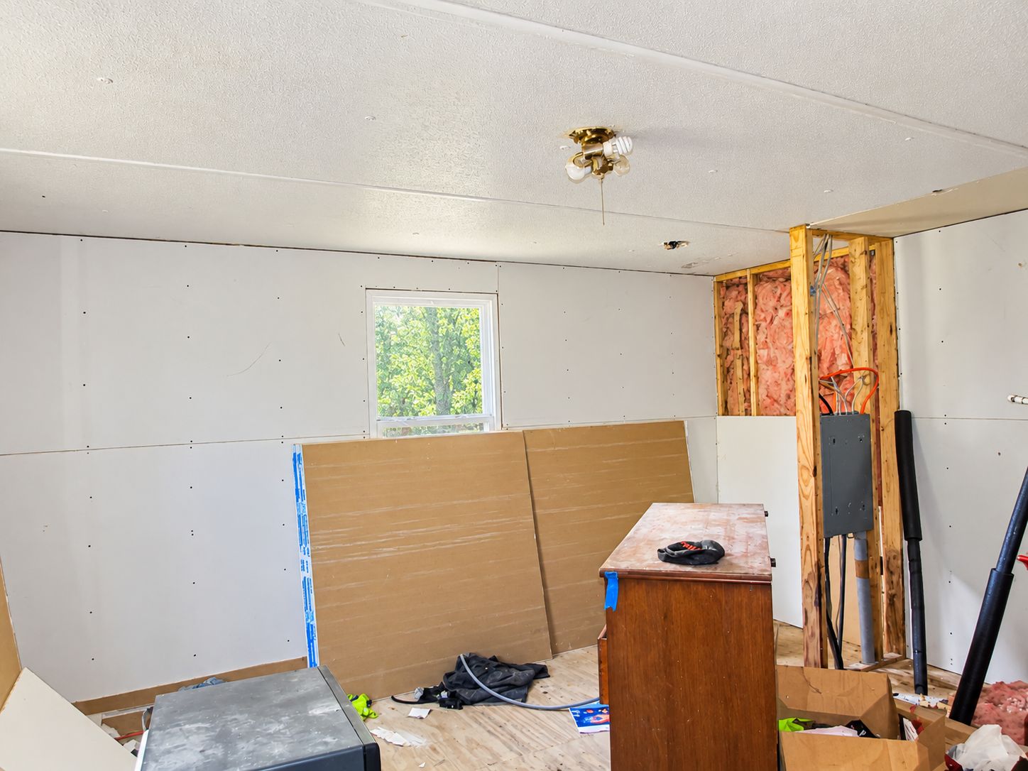 Partially renovated room with exposed insulation, plywood sheets, and construction tools on a counter.