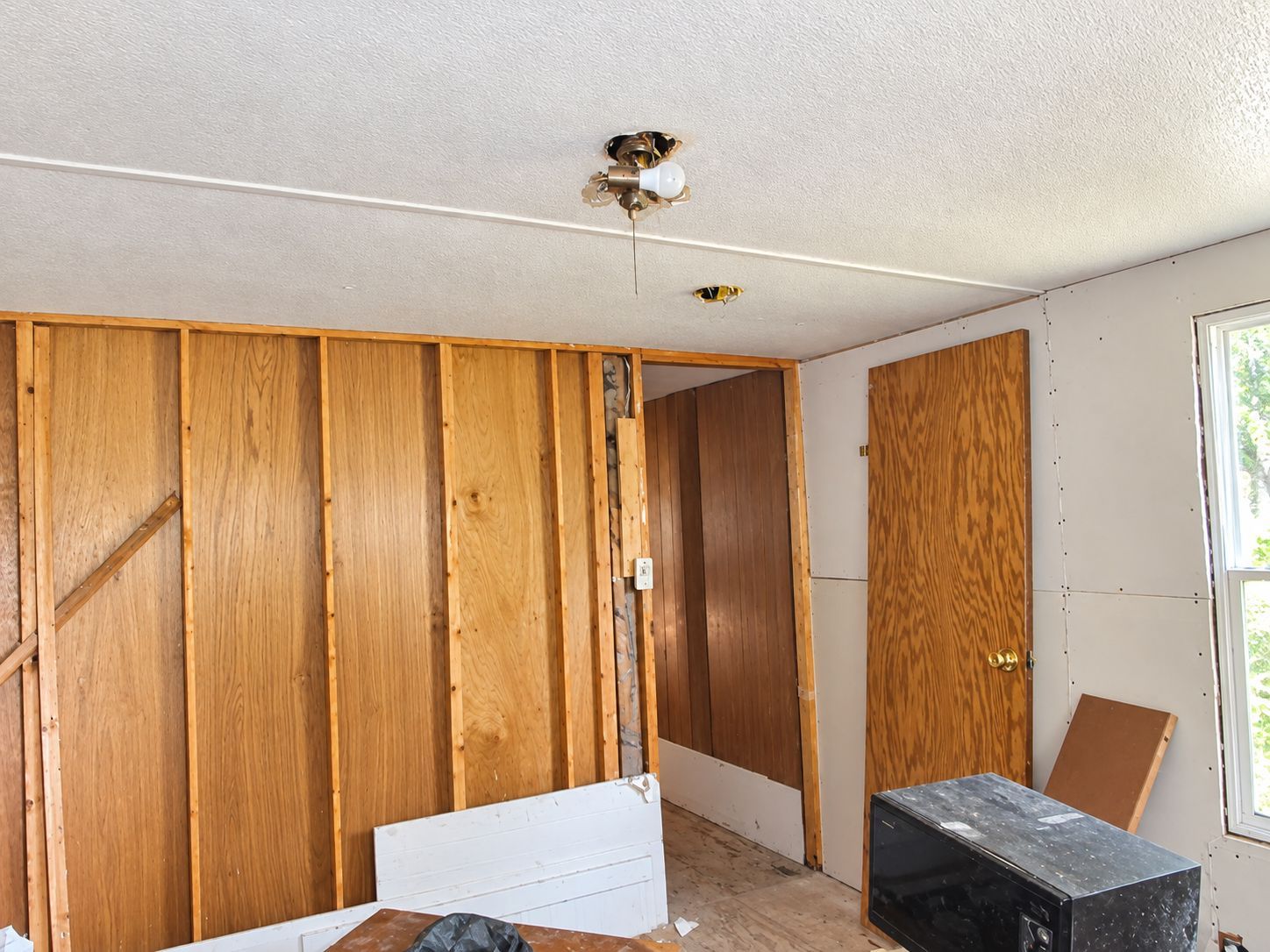 Empty room with wood-paneled walls, white ceiling, and a small window on the right.