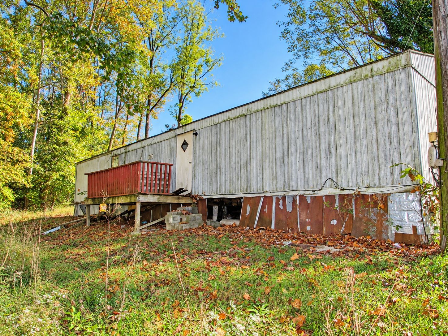 Old weathered white barn with red outbuilding amid autumn trees and grass