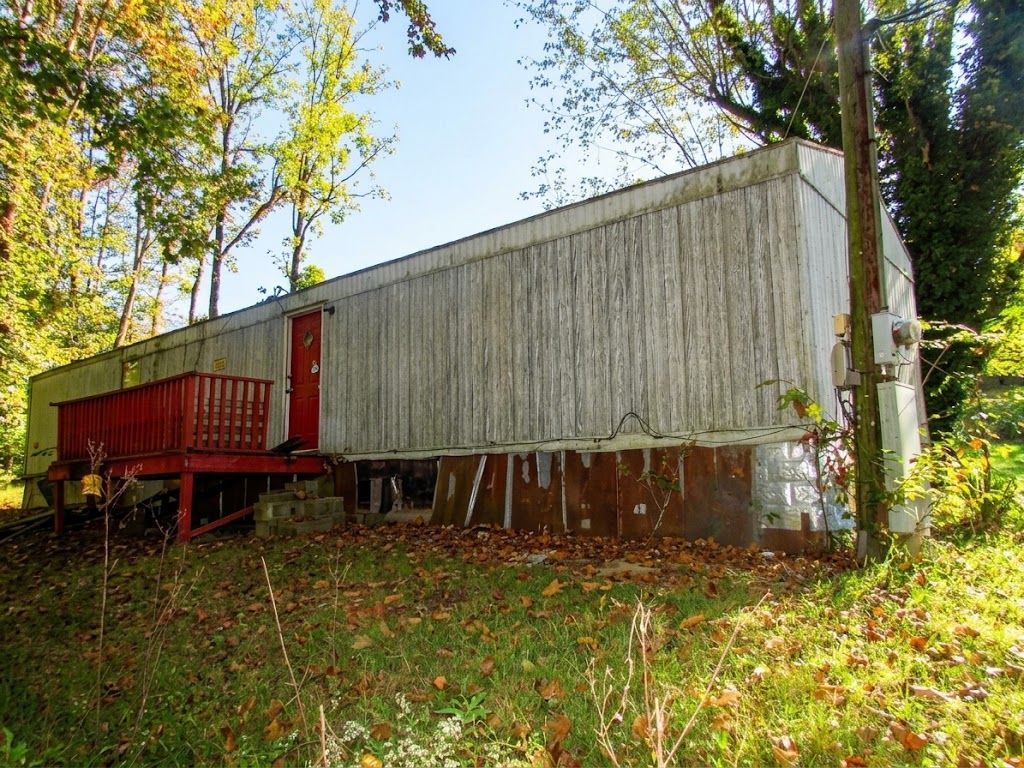 Red and white mobile home in a wooded yard with autumn leaves.