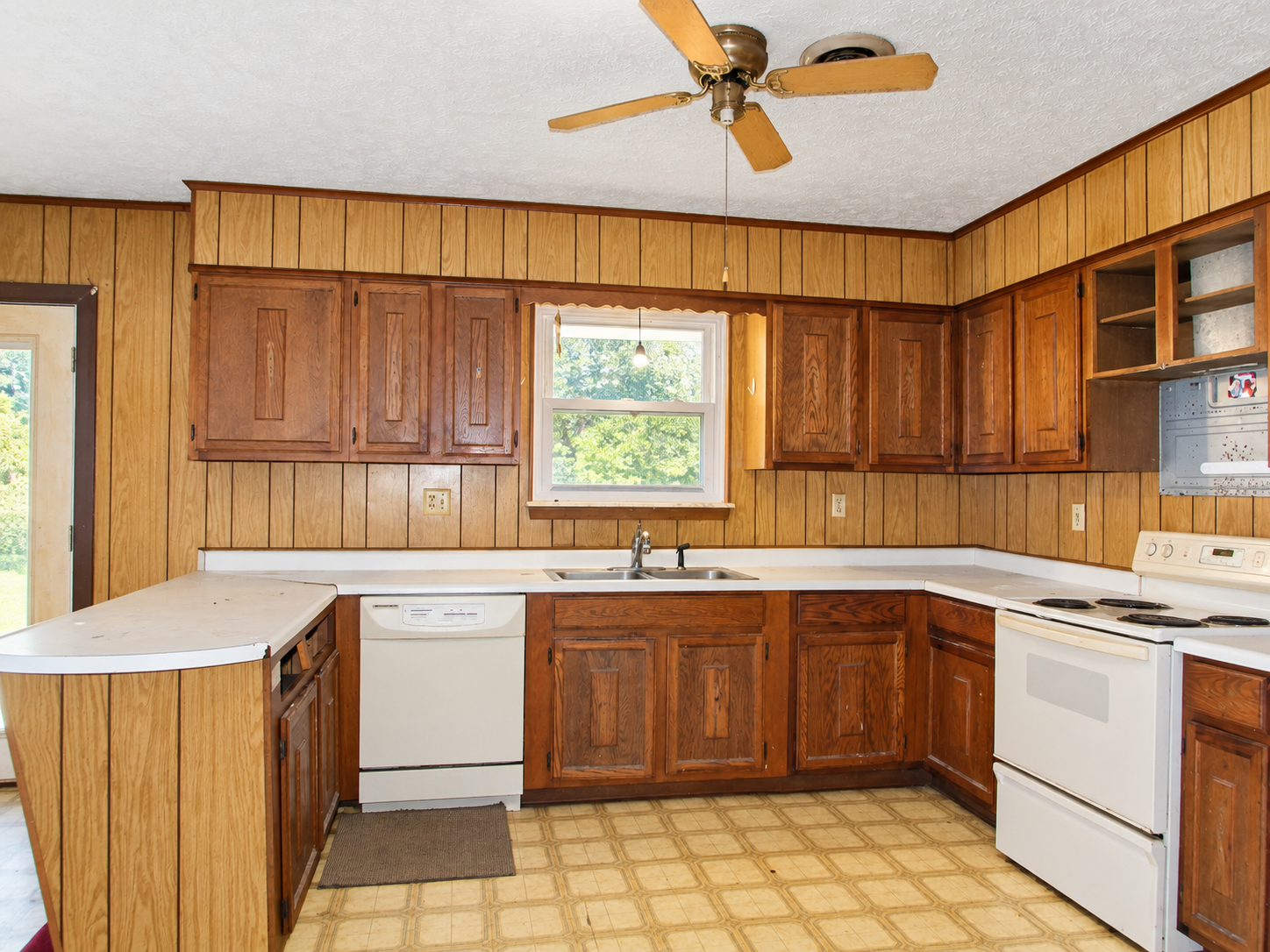 U-shaped kitchen with wood cabinets, white countertops, and a ceiling fan, lit by a central window
