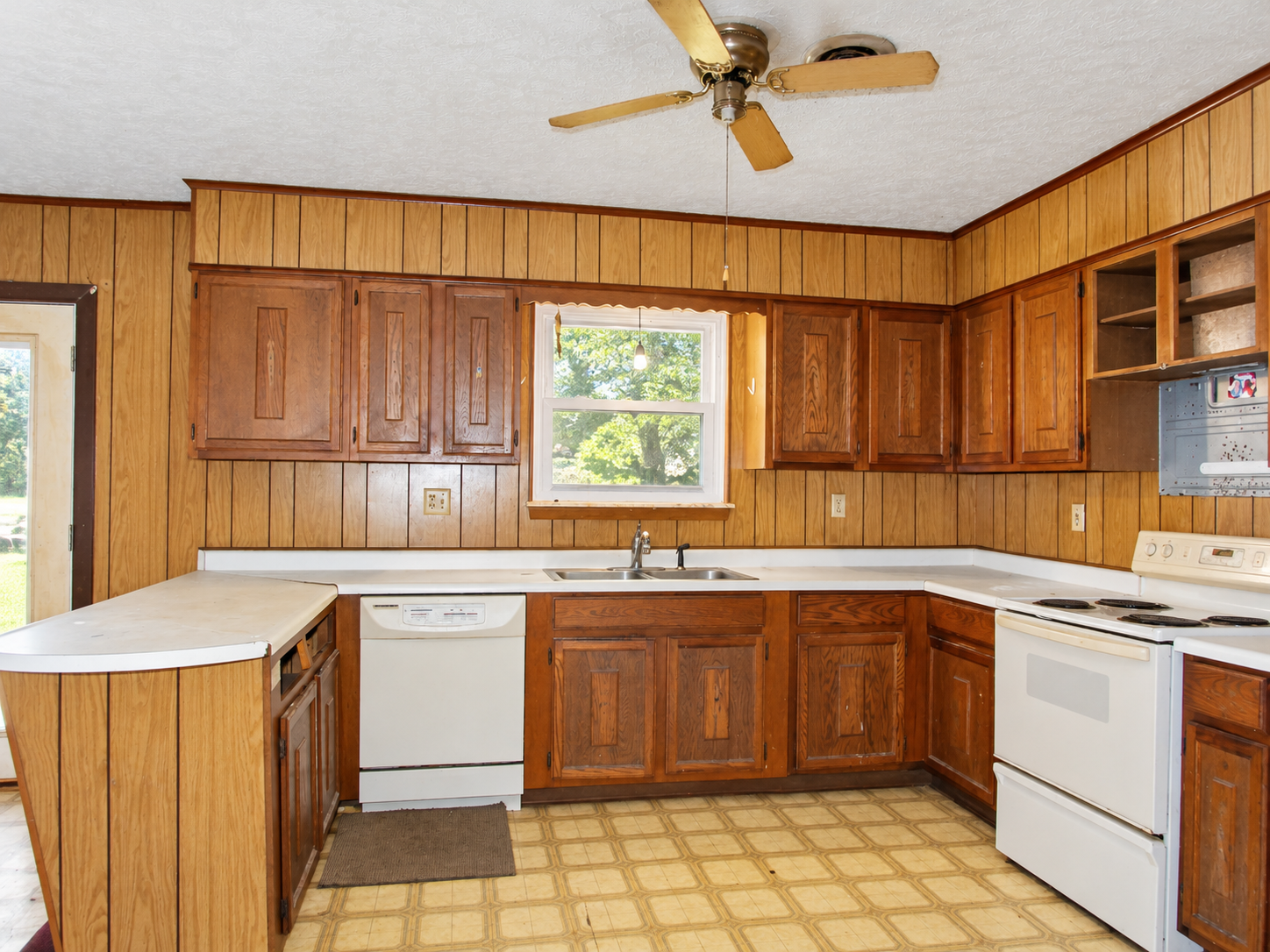 Empty kitchen with wood cabinets, white countertops, and a white dishwasher and stove.