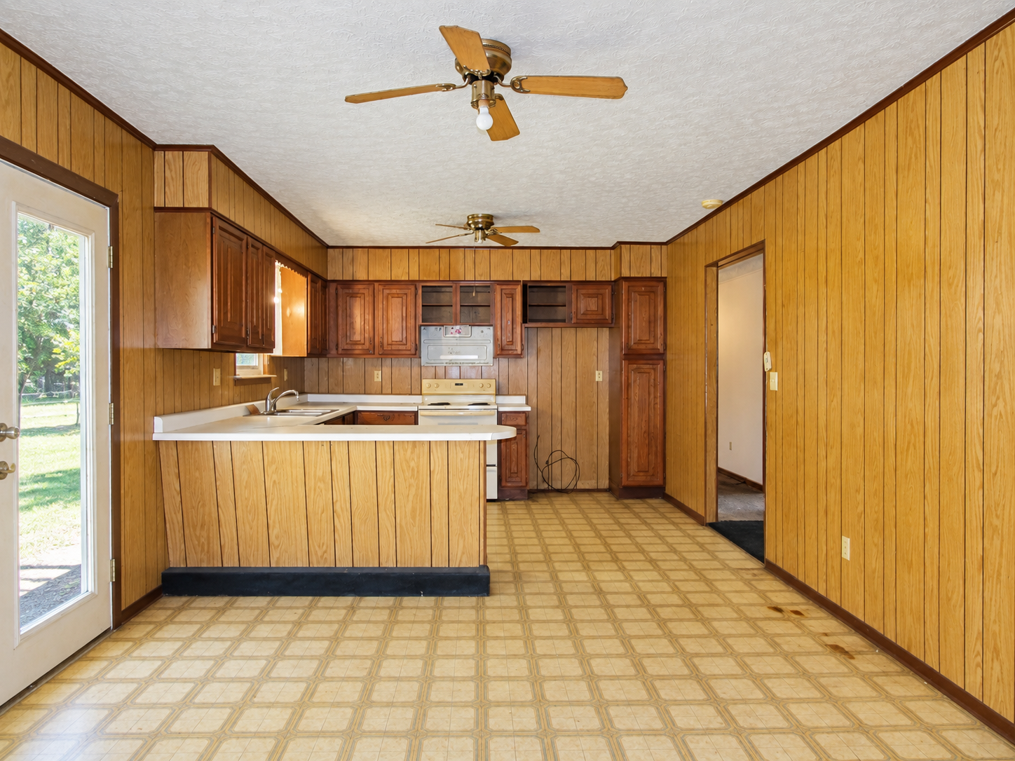 Empty wood-paneled kitchen with checkered floor, ceiling fans, and a pass-through counter.
