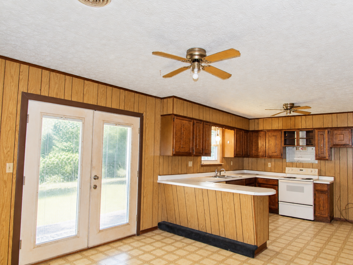 Wood-paneled kitchen with white appliances, island, and glass double doors to outside