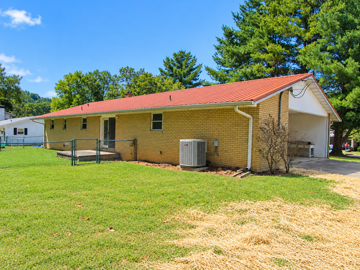 Single-story brick house with a red metal roof, white garage, and green lawn under a blue sky