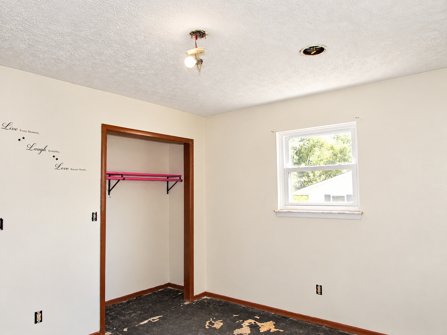 Empty bedroom with white walls, open closet, and a small window above carpet remnants