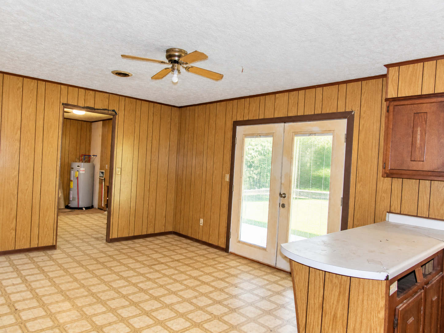 Empty wood-paneled kitchen with tan floor, ceiling fan, and glass double doors to outside.
