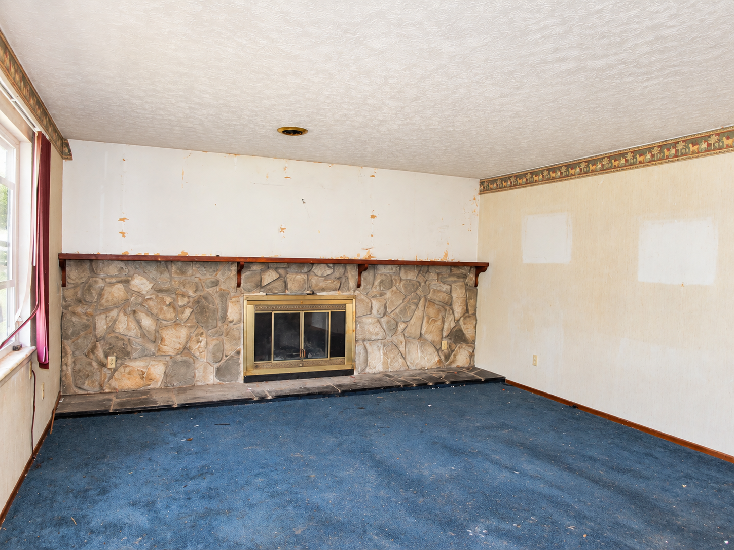 Empty living room with blue carpet, stone fireplace, and white walls