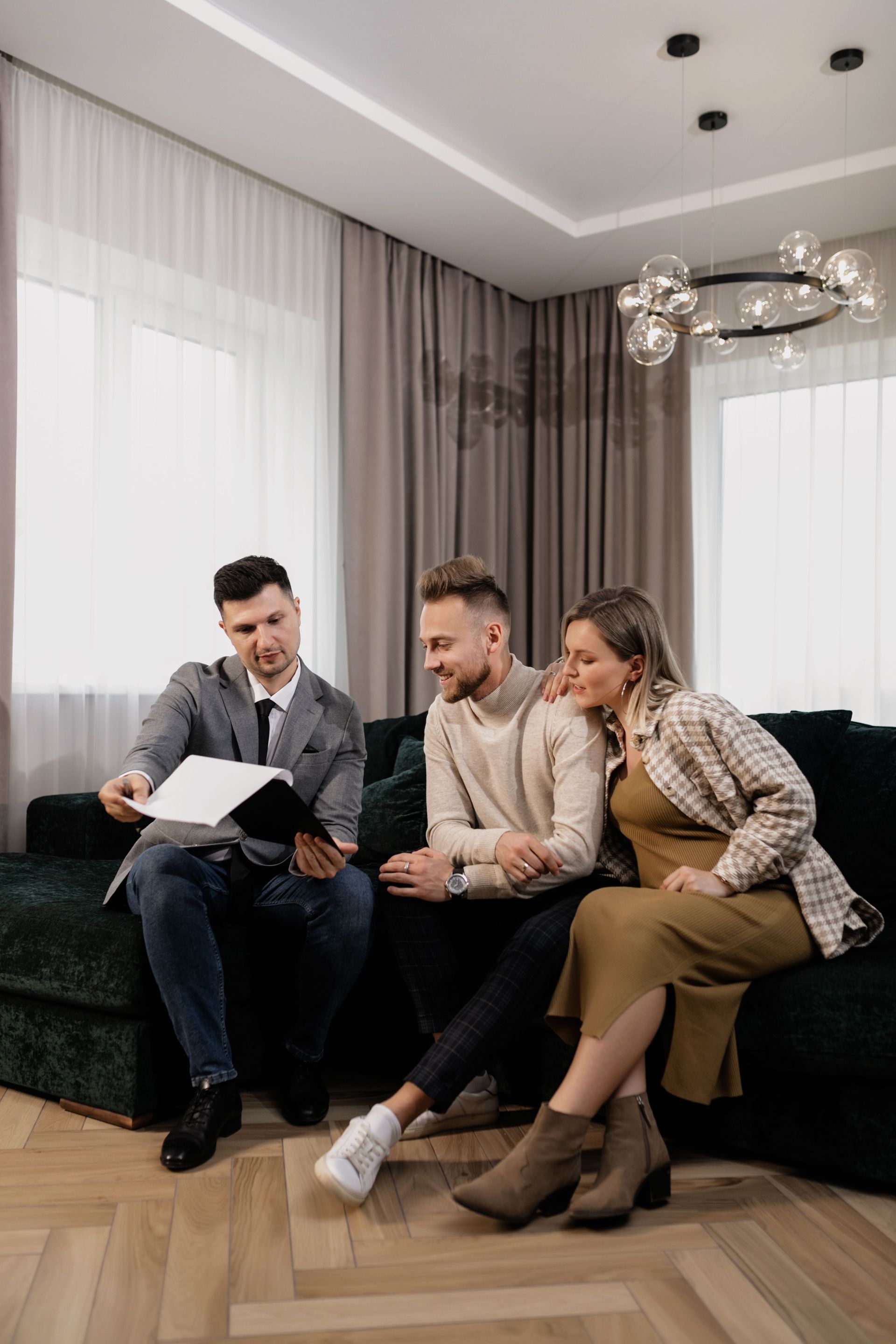 Three people sitting on a dark sofa, looking at a document in a bright modern living room