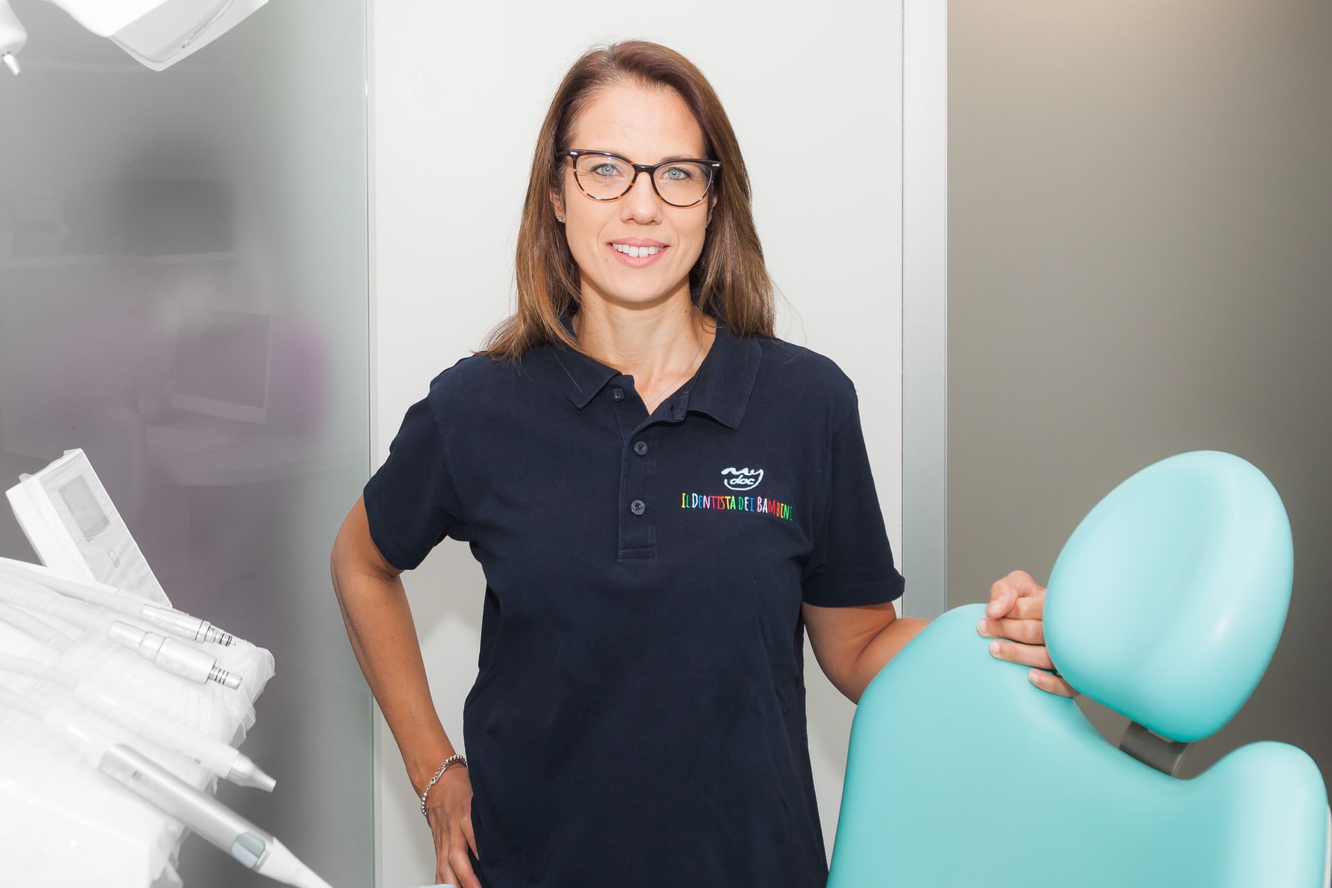 Una donna è in piedi in uno studio dentistico accanto a una poltrona.