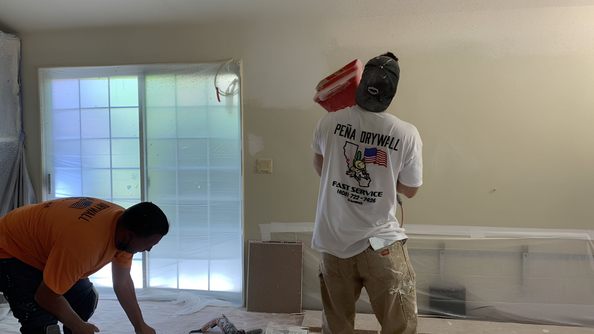 Two people working on a room interior, one bending near the floor and one standing by a wall.