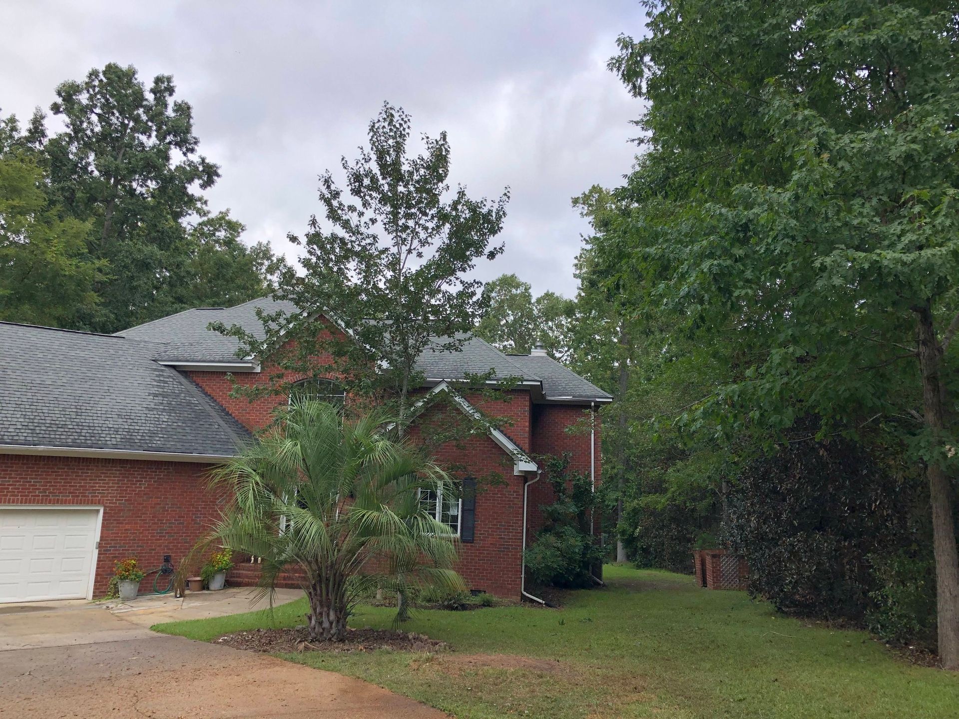 Red brick house with gray roof and white garage door, surrounded by trees and a grassy yard.