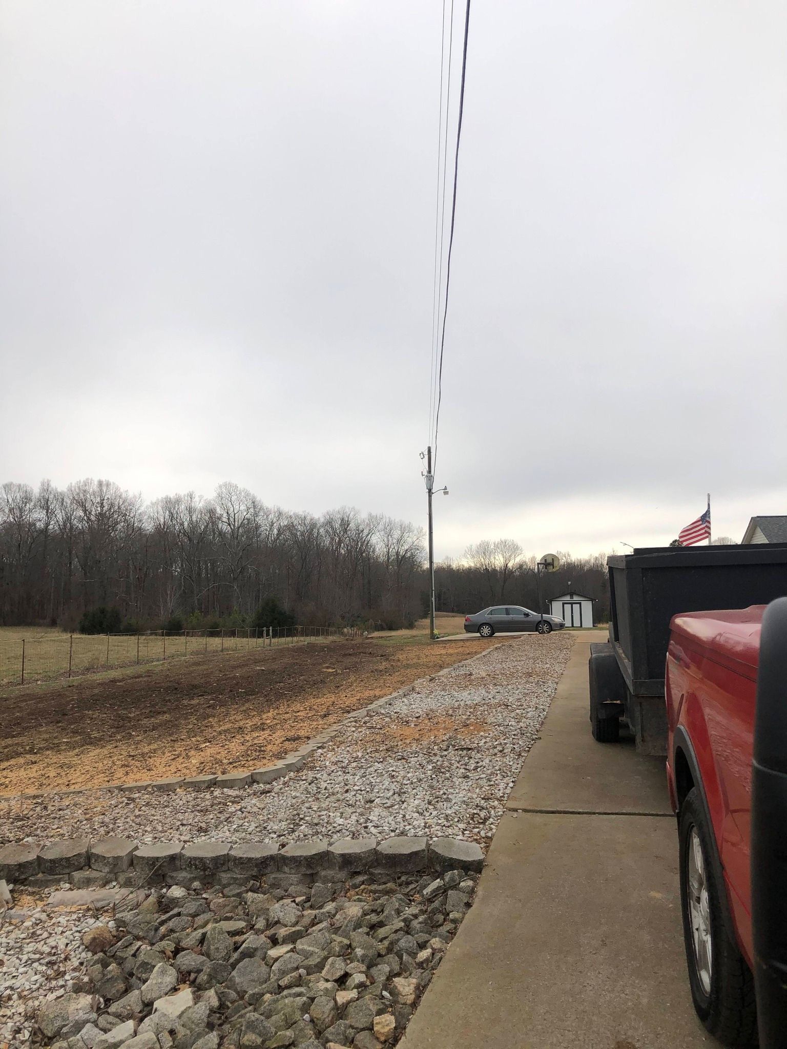 Gravel path beside an empty field under a gray sky, with a red truck at right.