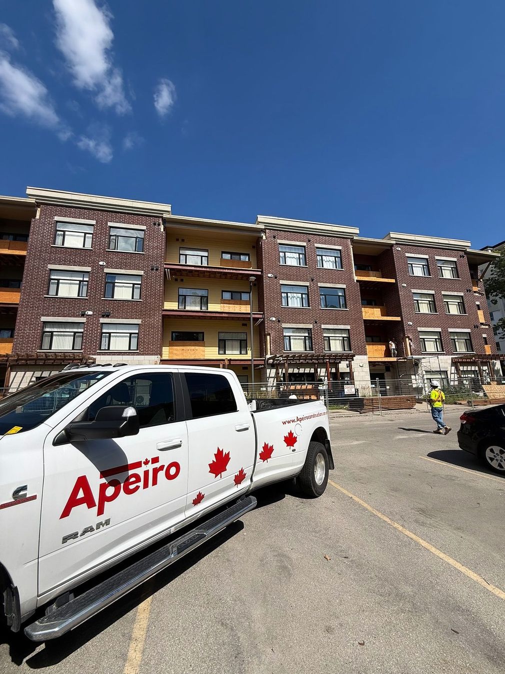 Apartment building with a white Apeiro pickup truck parked in front under a blue sky