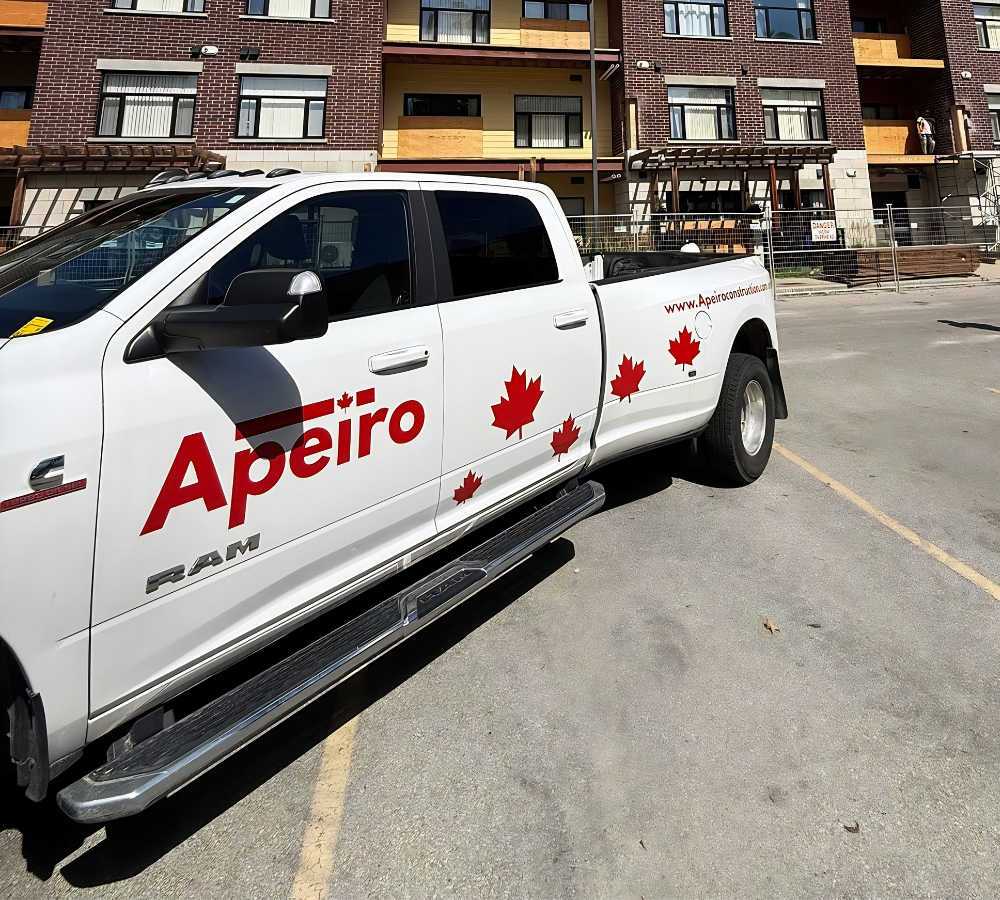 White Apero pickup truck with red maple leaves parked on a city street beside apartment buildings