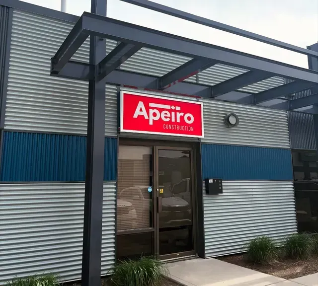 Apeiro storefront with red sign above a glass entrance and blue-and-gray metal exterior panels
