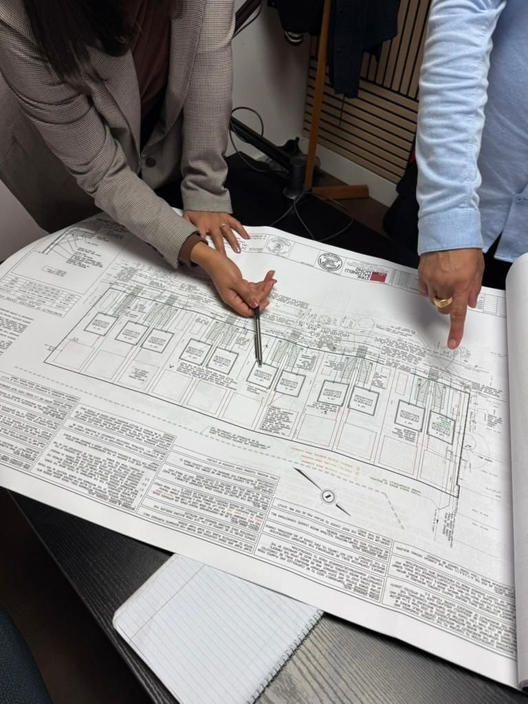 Two people point at a large printed plan spread across a table in an office setting