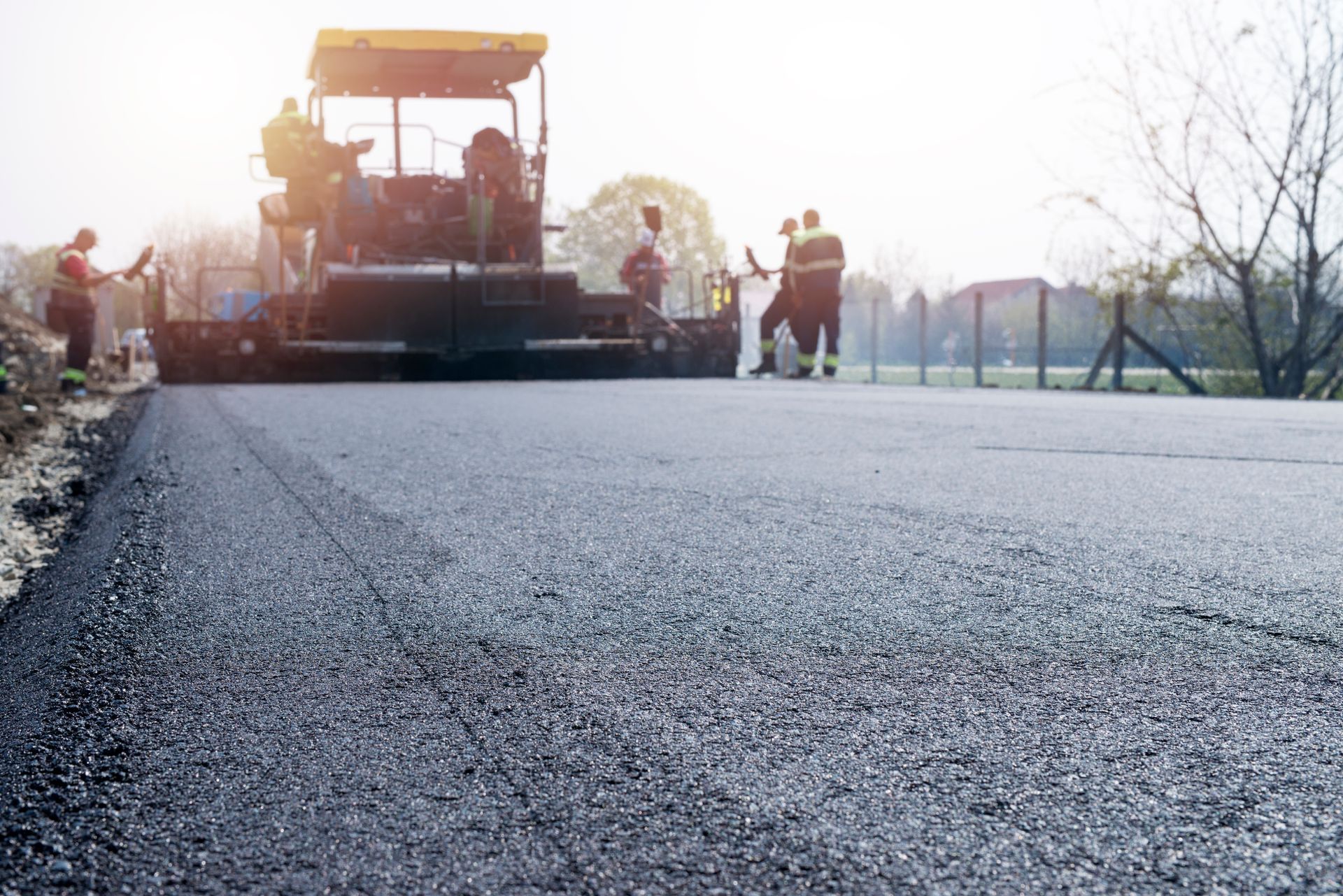 Road paving crew using a paver to lay fresh asphalt on a sunlit road
