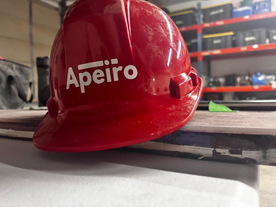 Red hard hat with “Apeiro” logo resting on a construction surface.