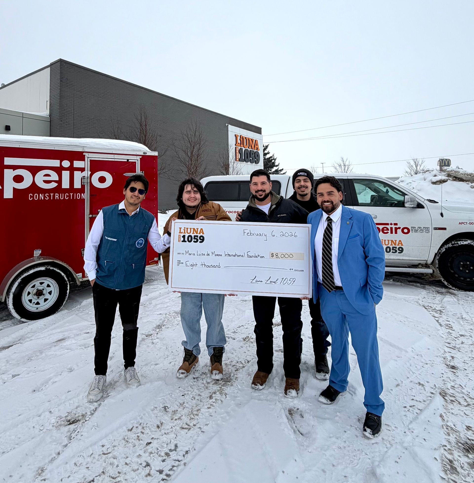 Four people holding a giant check in front of red and white Peirol trucks on a snowy day